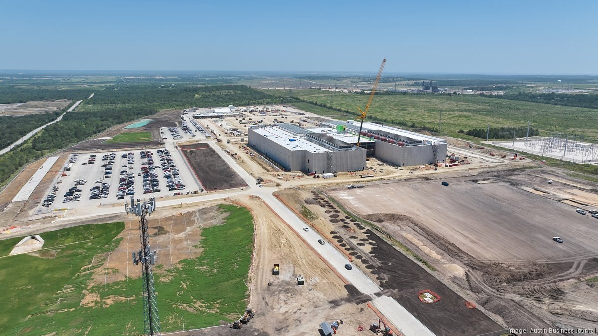 Aerial of the EdgeConneX Cedar Creek campus on July 20, 2026, showing tall plain concrete walls, rooftop equipment, a crane, a substation, construction parking and cleared land.